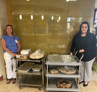 An Envista employee stands with an HRMC employee on either side of a breakfast cart.