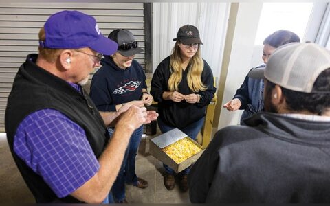 A feedlot production class taught by Mike Apley, DVM, evaluates a scoop of fresh steamed corn flakes during a visit to Knights Feedlot, Inc., near Lyons. Photo Credit: KSRE