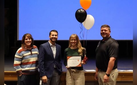 Megan Bloom is surrounded by 2 males and one female while she holds her plaque.